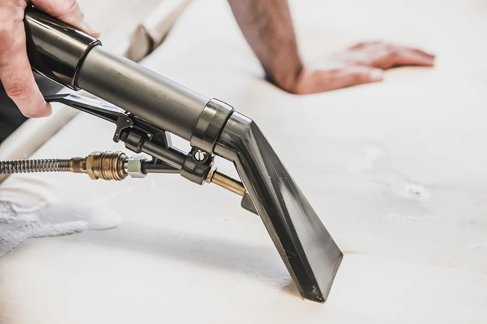 Upholstery extraction tool cleaning a light-colored upholstered surface.